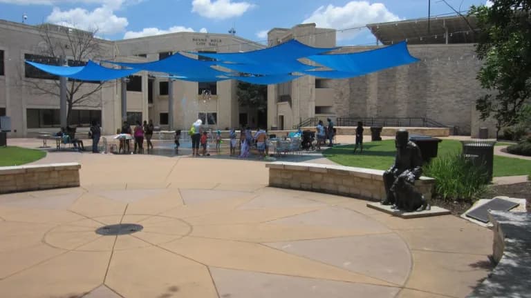 Main Street Plaza in downtown Round Rock with blue shade sails, a statue and people gathered