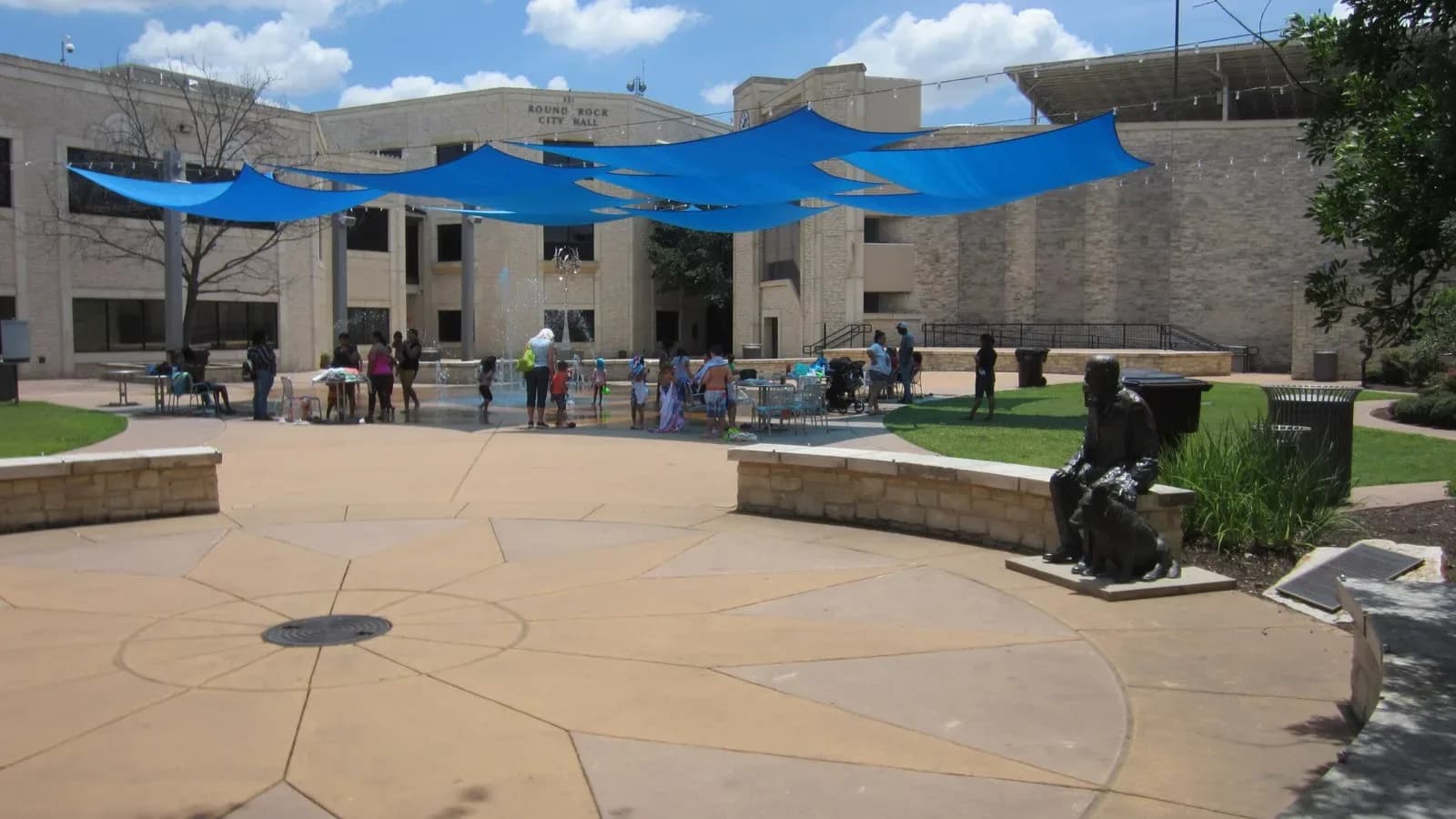 Main Street Plaza in downtown Round Rock with blue shade sails, a statue and people gathered