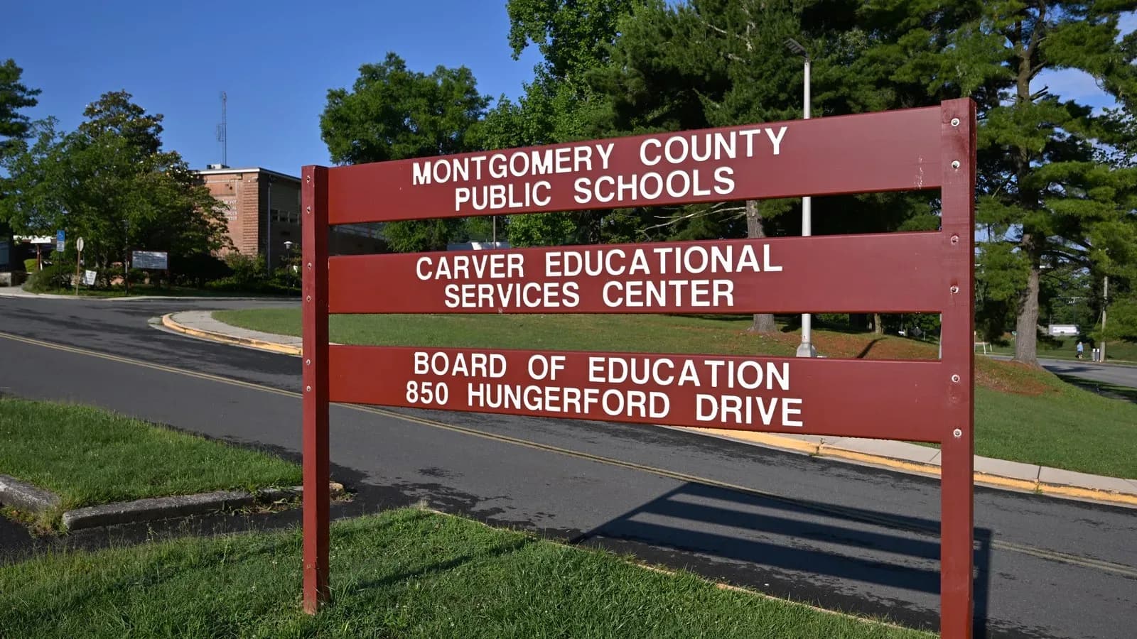 A red wooden sign reading Montgomery County Public Schools, Carver Educational Services Center, Board of Education, 850 Hungerford Drive, beside a road and lawn