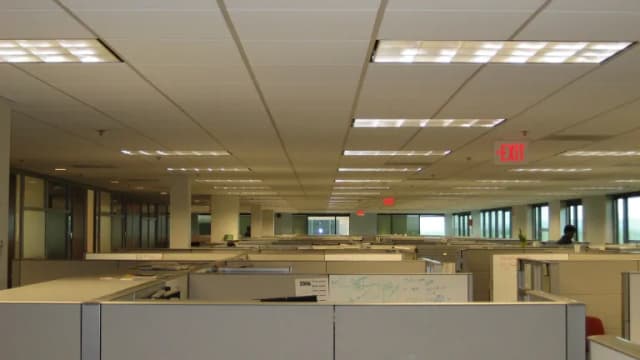 Rows of empty beige office cubicles stretching toward windows under fluorescent ceiling lights