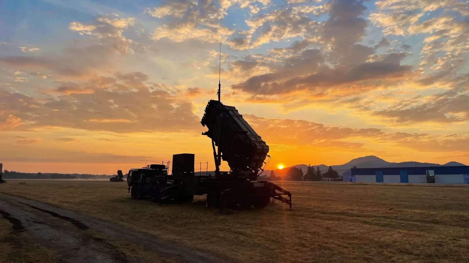 A Patriot missile launcher silhouetted on a flat field against an orange sunrise sky
