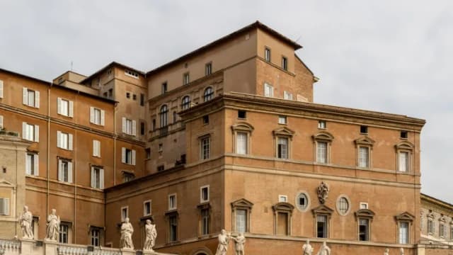 Tan stone Vatican palace buildings with rows of windows and statues along a colonnade above St. Peter's Square