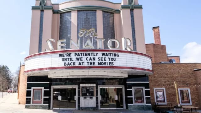 The Art Deco Senator Theatre in Baltimore with its marquee reading We are patiently waiting until we can see you back at the movies