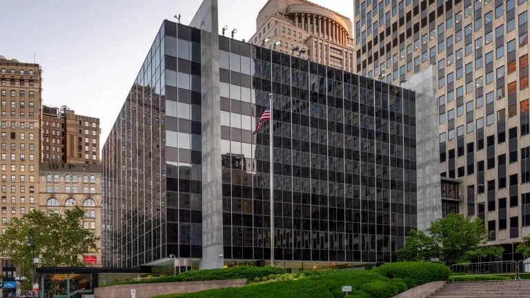 A dark glass federal office tower with an American flag in front, set behind a landscaped plaza in lower Manhattan