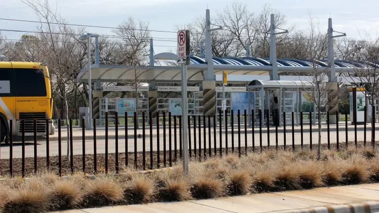 The Farmers Branch DART station platform behind a fence with a bus at left