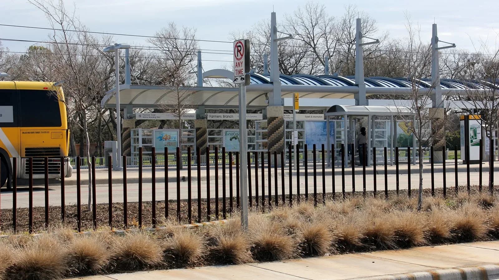 The Farmers Branch DART station platform behind a fence with a bus at left