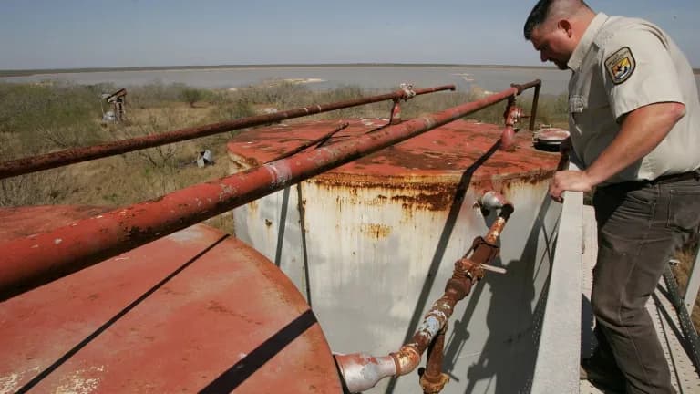 A refuge officer inspects rusted tanks and pipes at an abandoned oil well site