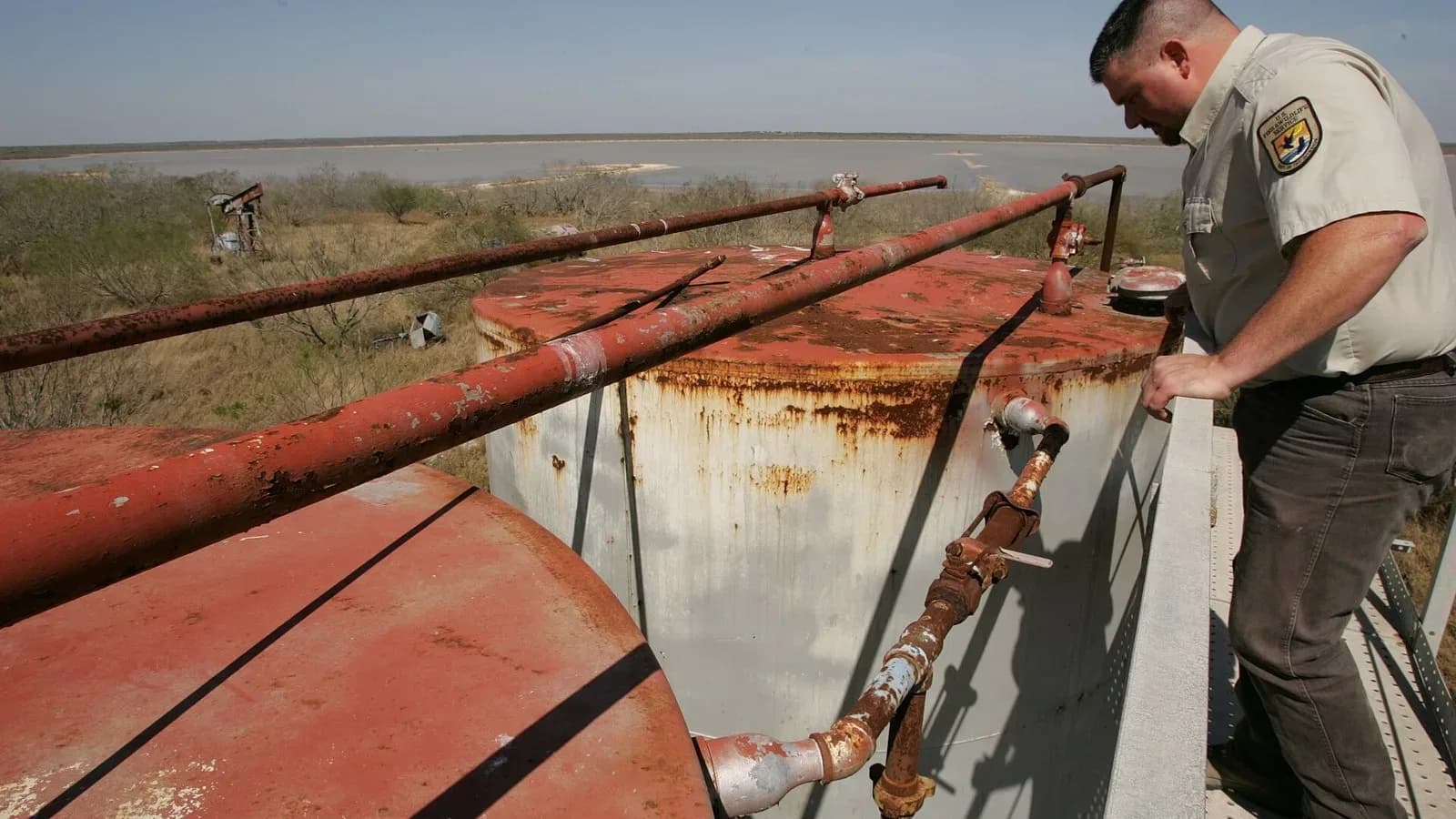 A refuge officer inspects rusted tanks and pipes at an abandoned oil well site
