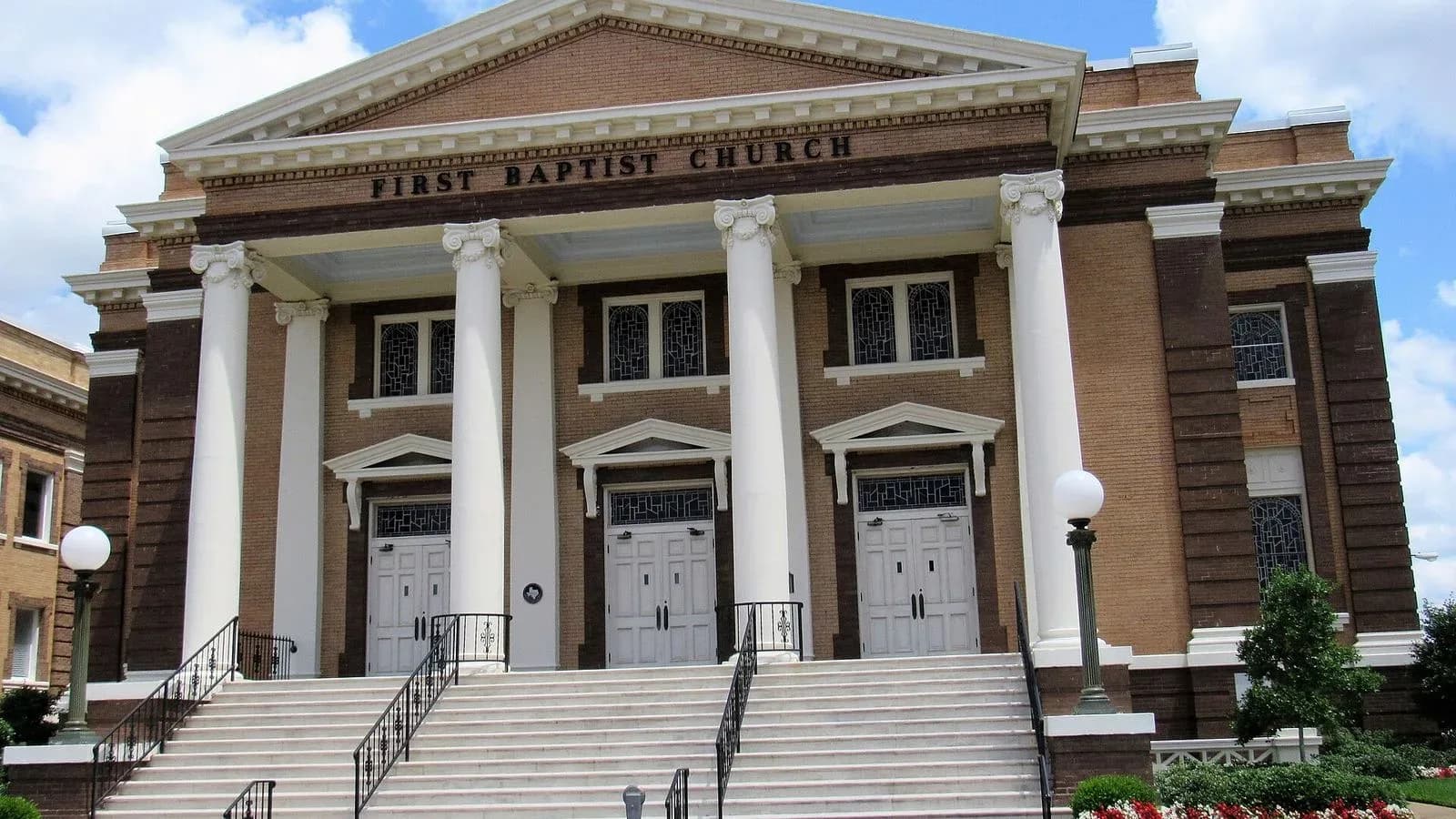 A brick First Baptist Church building with tall white columns and wide front steps