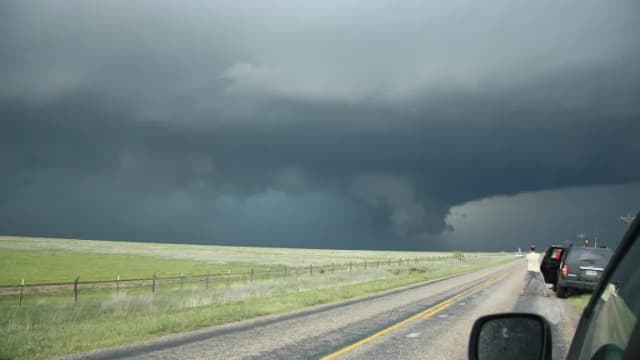 A dark storm cloud over green grassland beside a rural highway in the Texas Panhandle