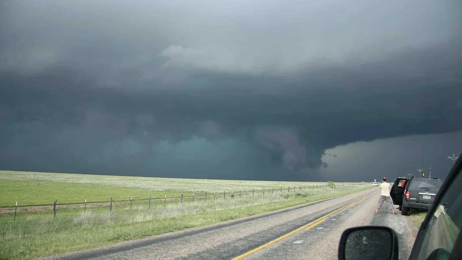 A dark storm cloud over green grassland beside a rural highway in the Texas Panhandle