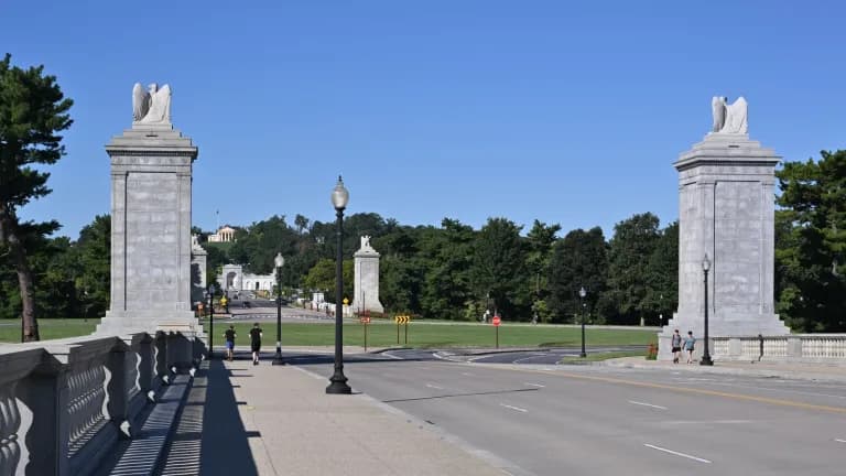 Granite pylons topped with eagle sculptures at the west end of Arlington Memorial Bridge, with Memorial Circle and Arlington House on the hill beyond