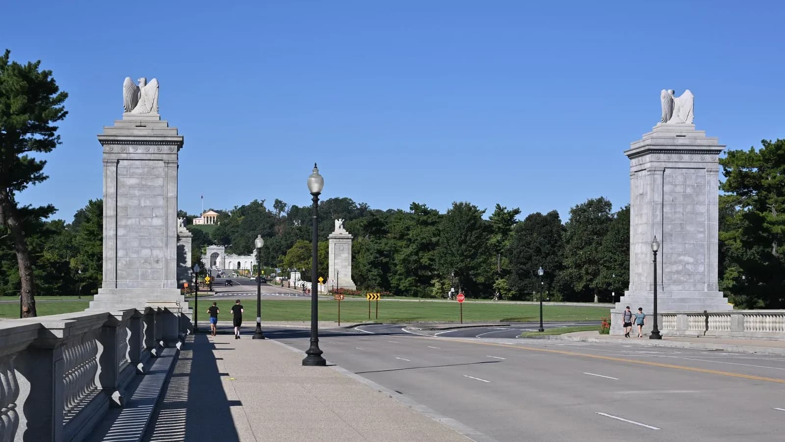 Granite pylons topped with eagle sculptures at the west end of Arlington Memorial Bridge, with Memorial Circle and Arlington House on the hill beyond