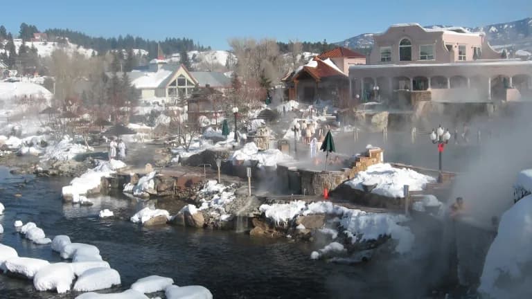 The San Juan River running past steaming hot springs pools and snow-covered rocks in Pagosa Springs, Colorado, under a blue sky