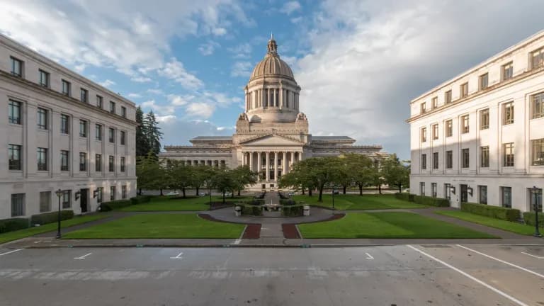 The domed Legislative Building of the Washington State Capitol in Olympia, flanked by office buildings, behind a lawn and fountain plaza