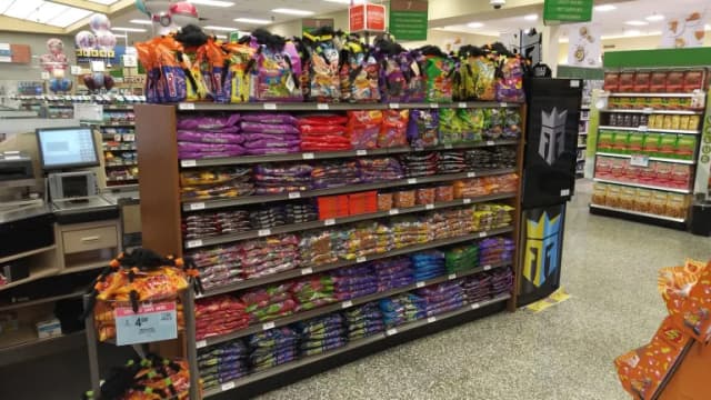 Shelves stocked with bags of Halloween candy near the checkout lanes of a grocery store, with seasonal displays on top