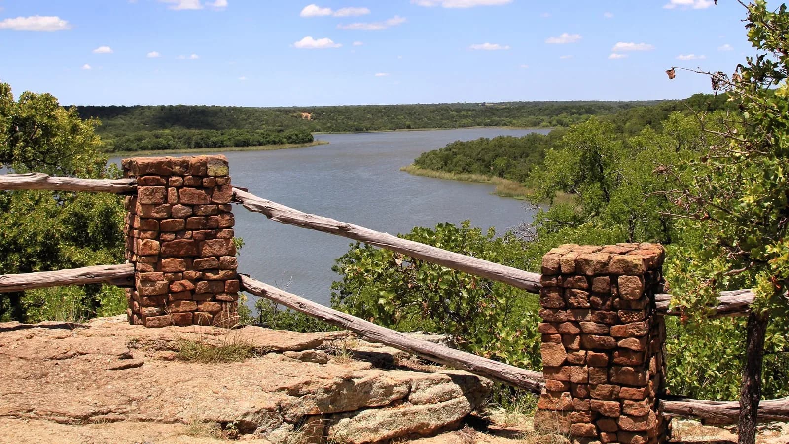 A rustic stone-and-rail overlook above Lake Mineral Wells surrounded by green hills