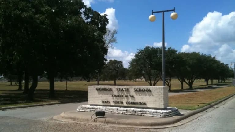 A stone entrance sign for Giddings State School, bearing the Texas Youth Commission name, with oak trees behind