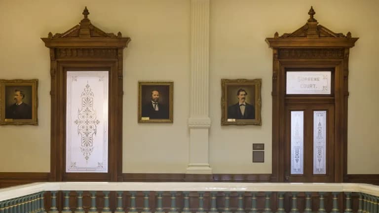 Two carved wooden doorways and framed portraits outside the historic Supreme Court chamber in the Texas Capitol