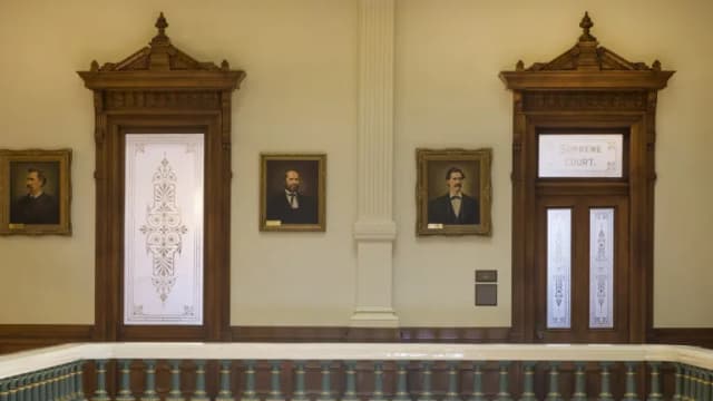 Two carved wooden doorways and framed portraits outside the historic Supreme Court chamber in the Texas Capitol