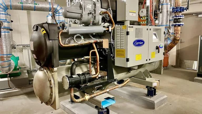 A Carrier-branded commercial chiller with copper piping in a building mechanical room