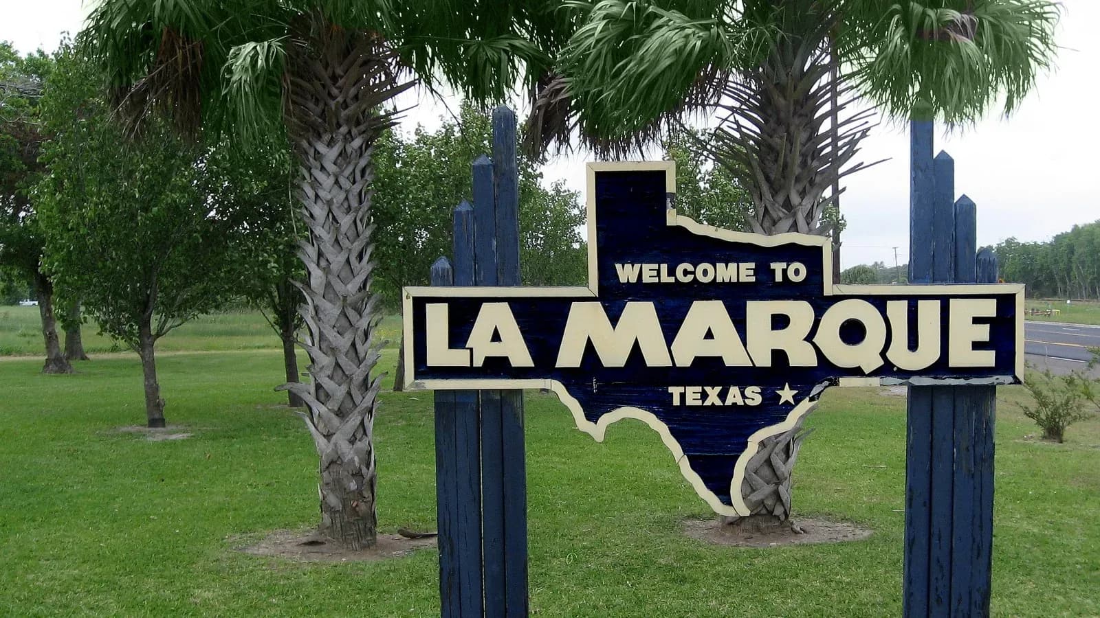 A Texas-shaped Welcome to La Marque sign between two palm trees