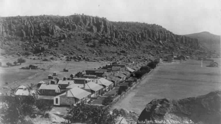 Black-and-white 1885 photograph of the Fort Davis army post seen from the south, with a long row of stone and adobe quarters along a wide parade ground at the foot of a steep cliff of tall rock columns