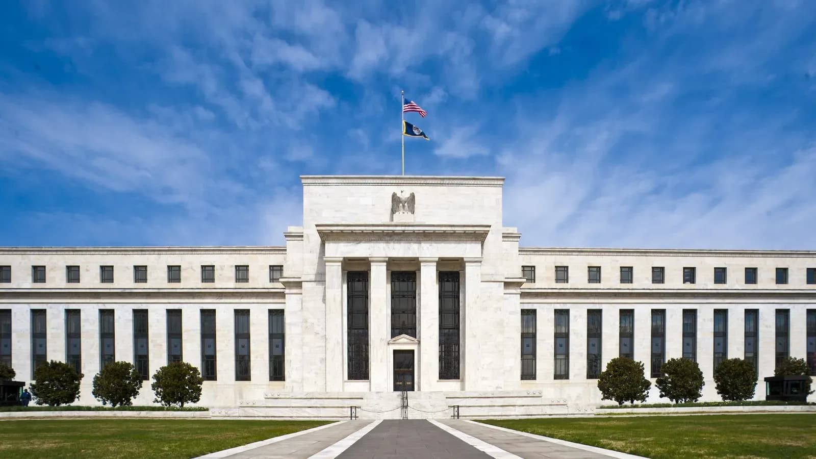 The white marble Eccles Building, headquarters of the Federal Reserve, under a blue sky with an American flag on top