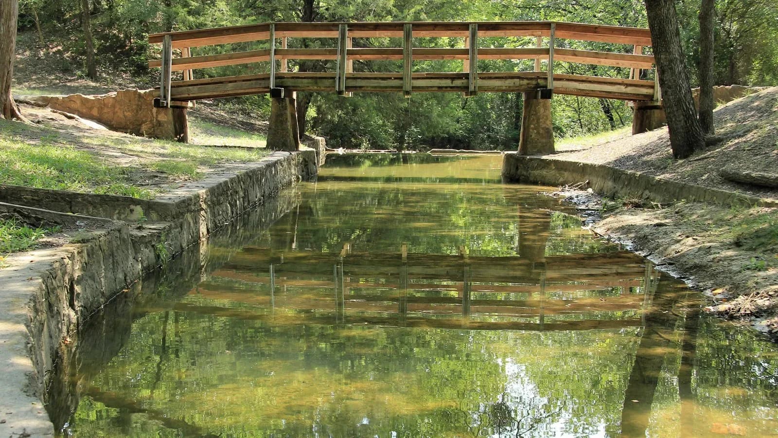 A wooden footbridge over a rock-lined channel at Grapevine Springs Preserve in Coppell, Texas