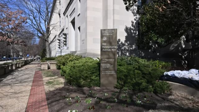 The corner of the Robert F. Kennedy Department of Justice Building in Washington, with its address sign among shrubs