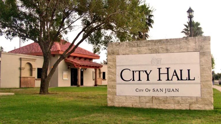 Stone City Hall sign in front of a tan building with a red tile roof in San Juan, Texas