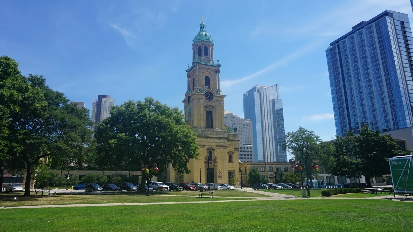 The bell tower of the Cathedral of St. John the Evangelist in Milwaukee beside a city park, with office towers behind