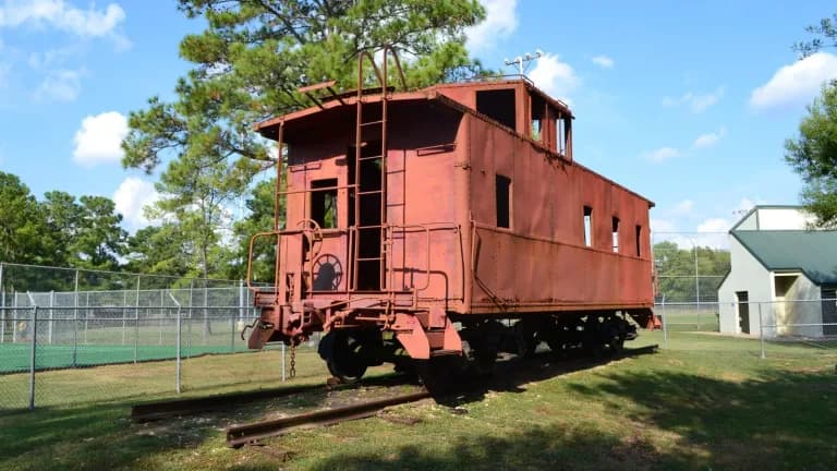 A red Southern Pacific caboose on display under trees at Crosby Park in Crosby, Texas