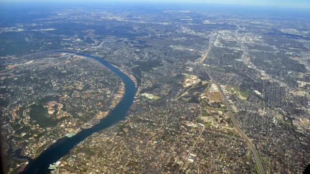 Aerial view of the Colorado River winding between wooded hills and neighborhoods west of Austin