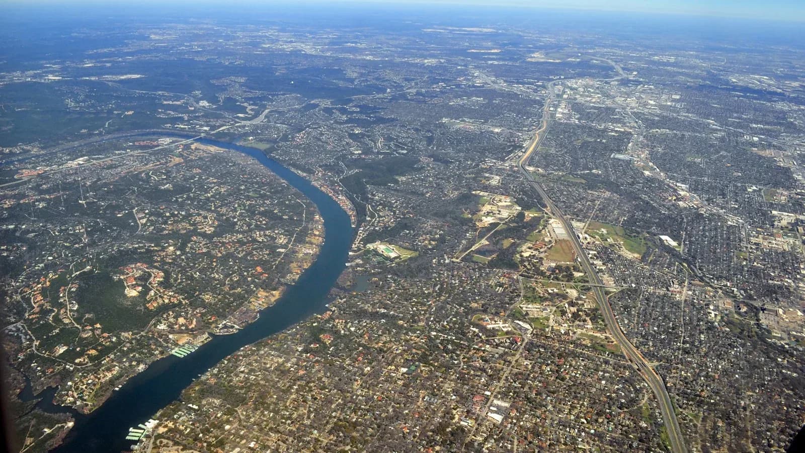 Aerial view of the Colorado River winding between wooded hills and neighborhoods west of Austin