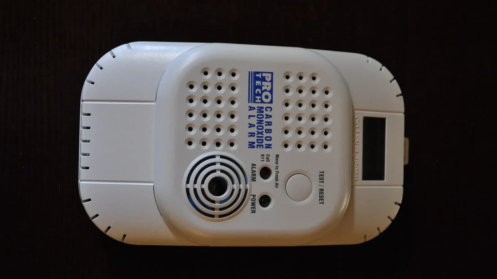 A white plug-in carbon monoxide alarm with a test button and digital display on a dark background