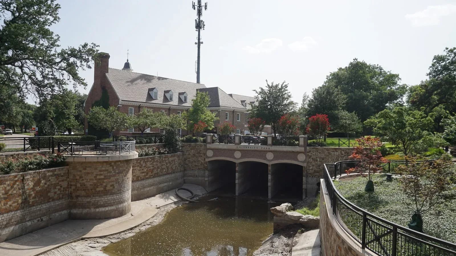 University Park City Hall, a red-brick building with dormers, behind a stone-walled creek channel and bridge