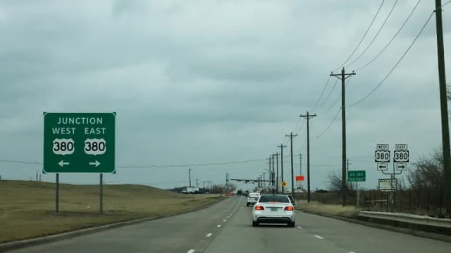 A four-lane road with a green Junction West East 380 sign and traffic heading toward U.S. 380 under a cloudy sky