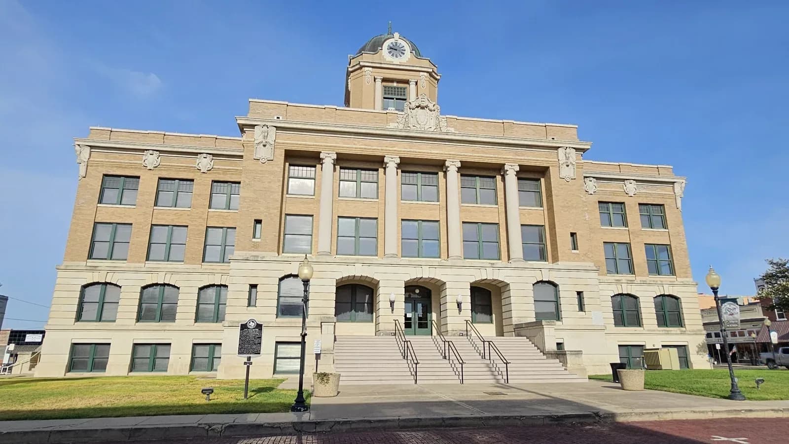 The tan stone Cooke County Courthouse in Gainesville with columns, a clock dome and a wide front staircase under a blue sky