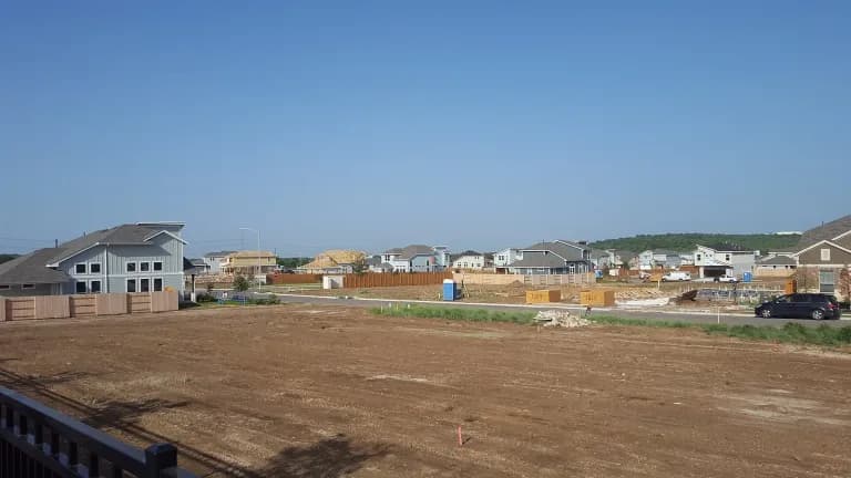 New houses and empty graded lots in a growing Austin subdivision under a clear sky