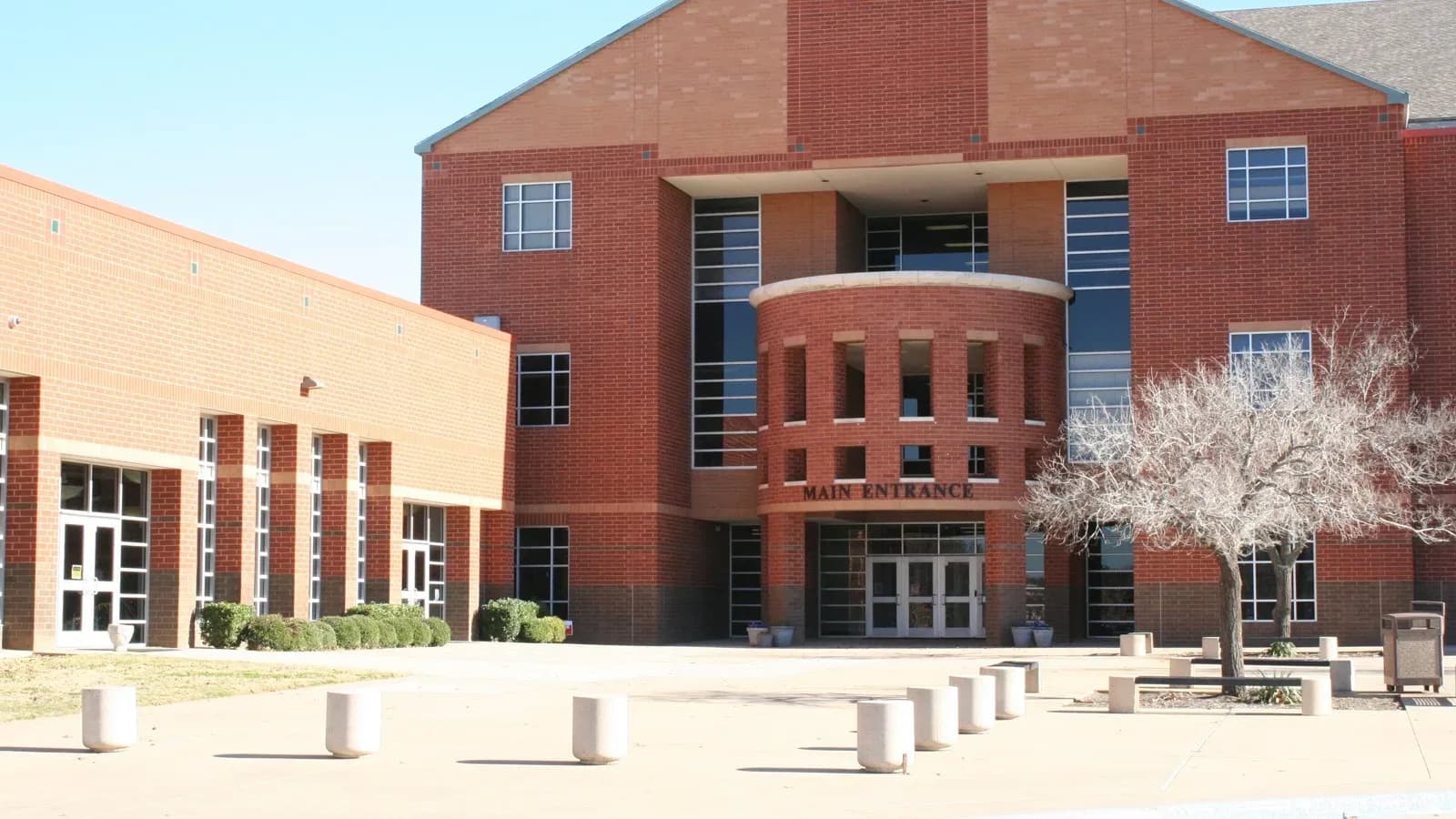 The red brick main entrance of Colleyville Heritage High School with a rounded tower, tall windows and concrete bollards