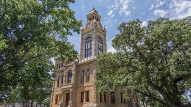 The sandstone Llano County Courthouse with its clock tower, framed by large oak trees