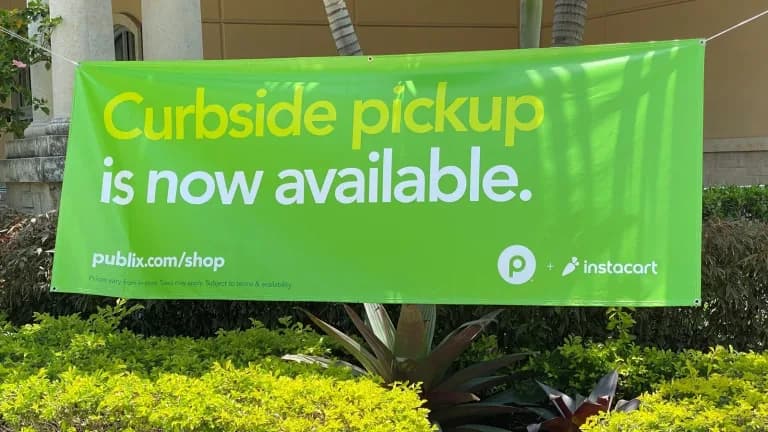 A green banner reading Curbside pickup is now available with Publix and Instacart logos outside a store in West Miami, Florida