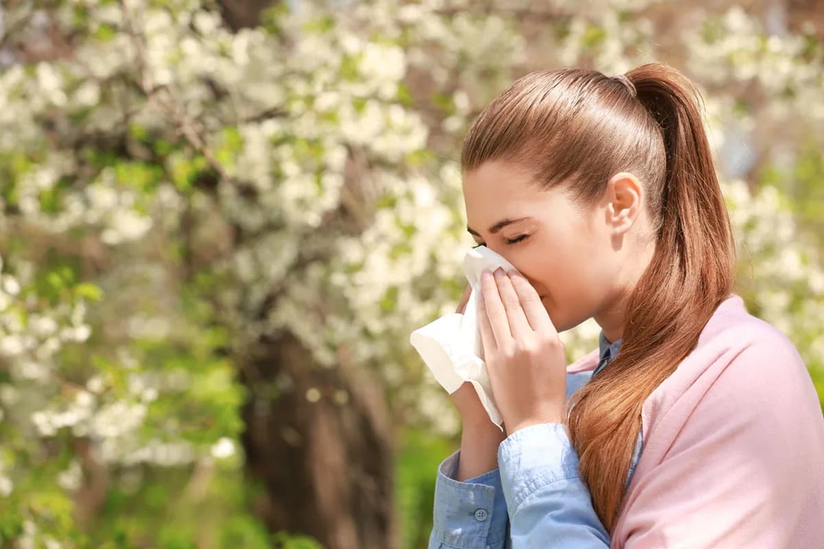 Sneezing young girl with nose wiper among blooming trees in park