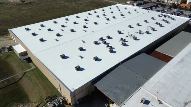 A large commercial building with a bright white flat roof, vents, and rooftop equipment.