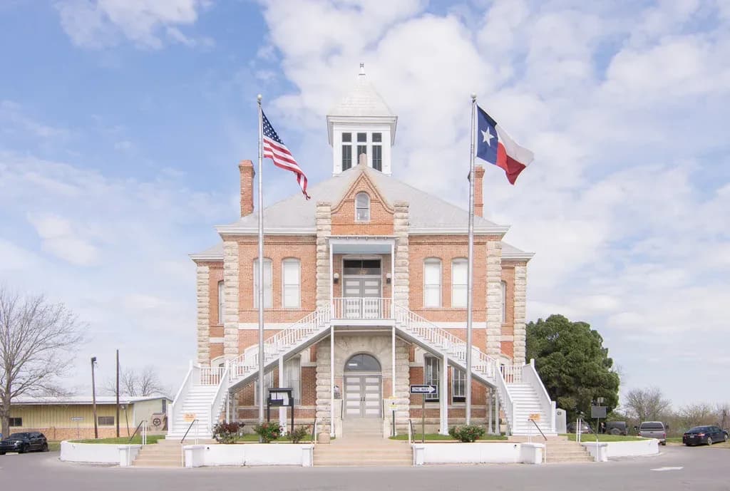 The brick Grimes County Courthouse in Anderson, Texas, with a double stair, a cupola, and the United States and Texas flags