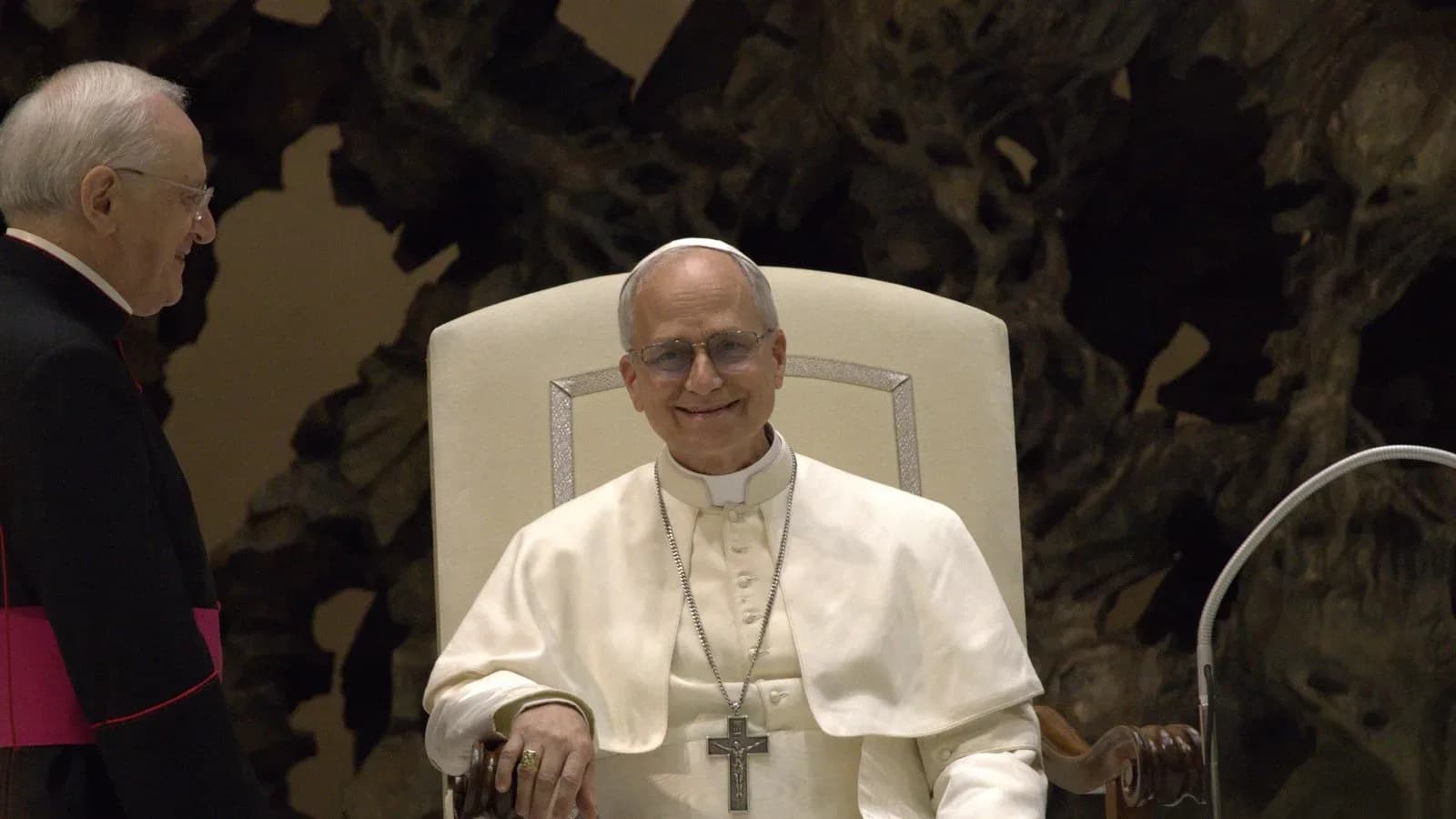 Pope Leo XIV, seated in white, smiling during an audience with the media