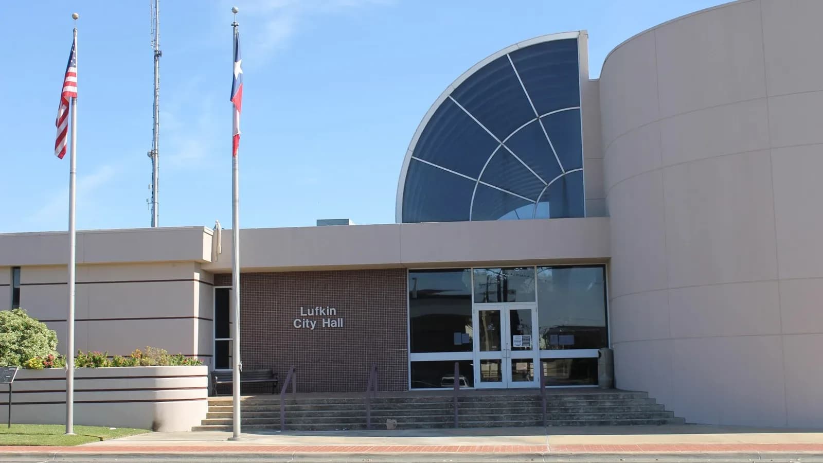 The front of Lufkin City Hall, with a curved glass entry and American and Texas flags on tall poles