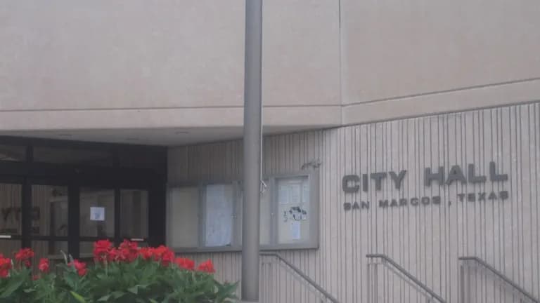 The entrance to San Marcos City Hall with the words City Hall San Marcos Texas on the wall and red flowers in front