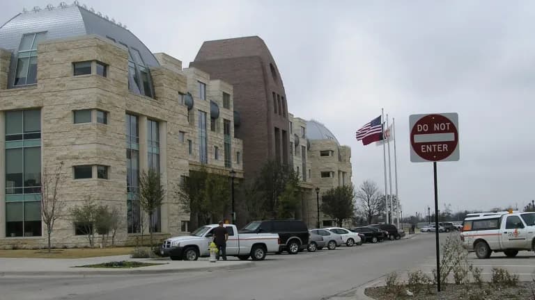 The tan stone Frisco City Hall with domed roofs and flags out front, beside a parking lot
